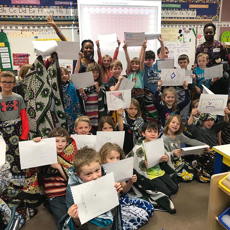 children in classroom holding up pieces of paper with drawn flags